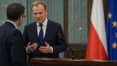 Wyłączony mikrofon na pulpicie, w tle rozmyta rozmowa polityków